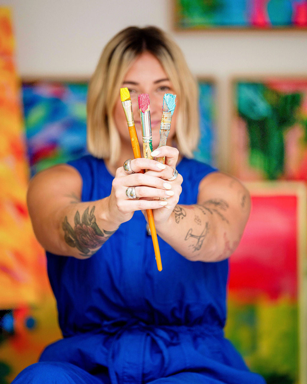 Person holding paintbrushes with colorful art in the background