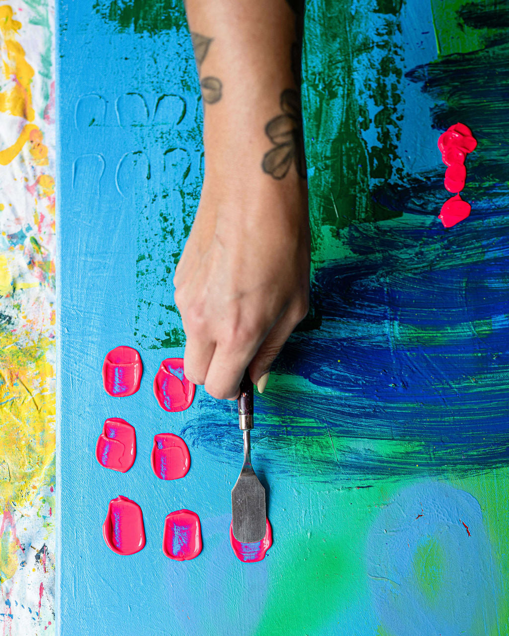 Hand with a tool working on a colorful painting with blue, green, and pink hues.