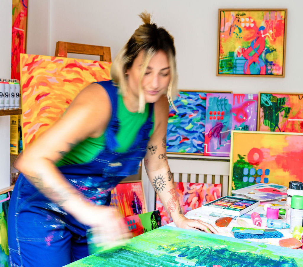 Person painting at a table with colorful art supplies and artworks on the wall.