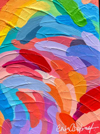 A framed abstract painting with thick, textured brushstrokes in a rainbow of colors including blue, red, orange, yellow, green, and purple, mounted on a textured brown wall.