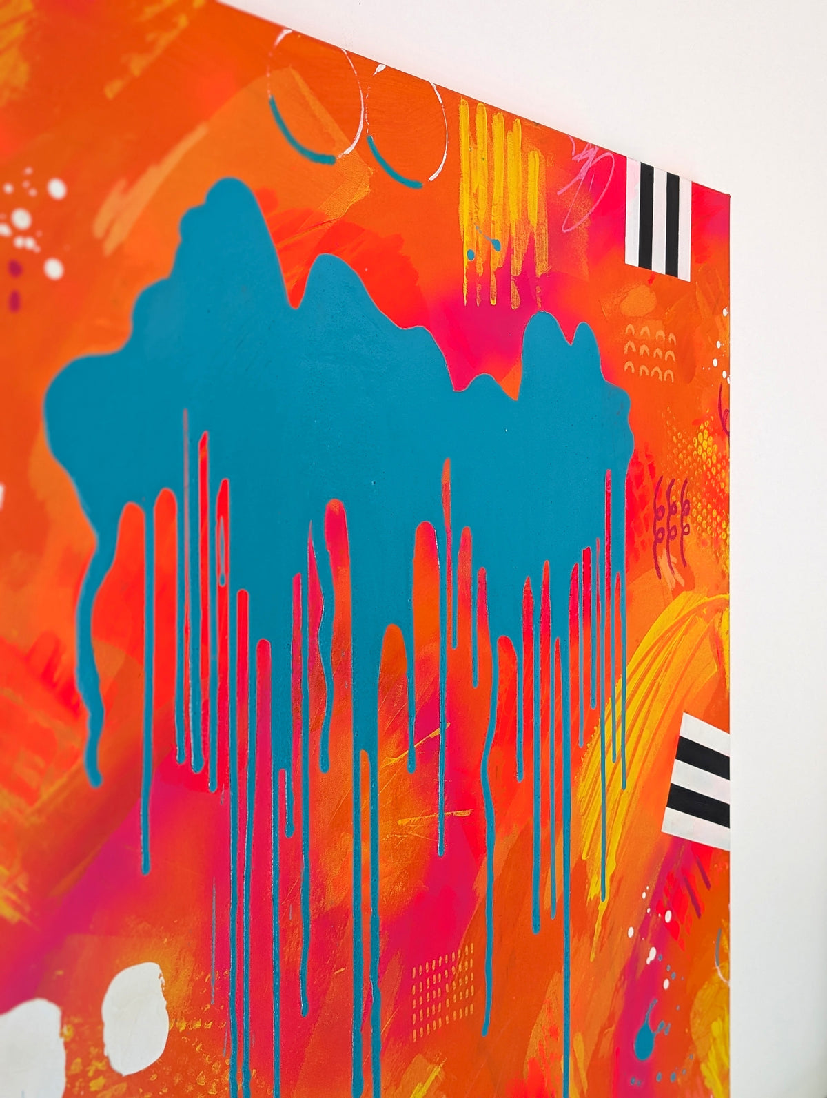 A close-up of a colorful abstract wall art print featuring a large blue paint drip over a bright orange, pink, and red background with yellow brushstrokes and black-and-white striped accents.